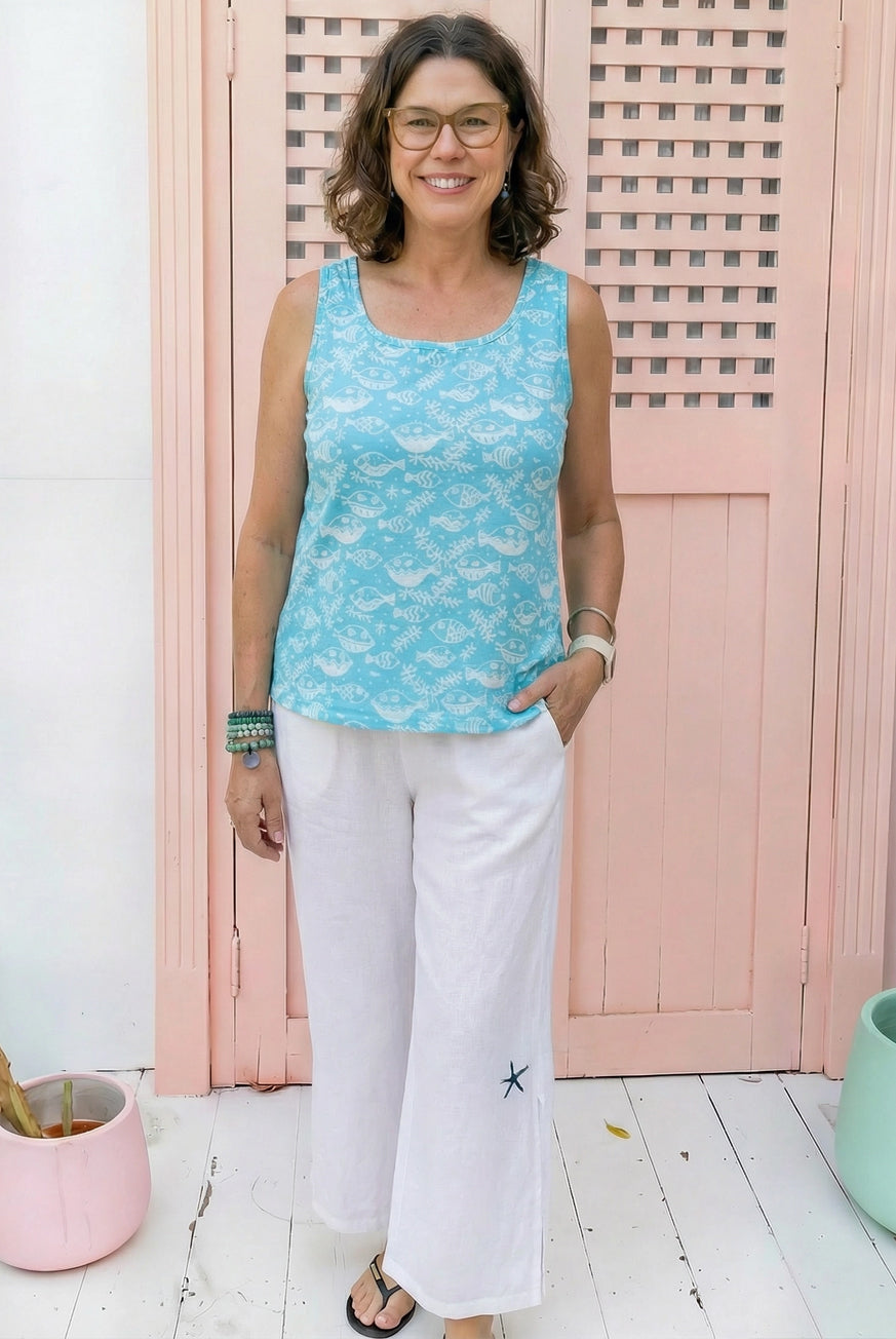 Woman wearing a blue sleeveless top and white pants standing in front of a pink wooden door.